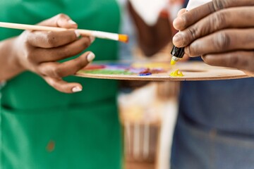 Hands of african american painter couple holding paintbrush and palette at art studio.
