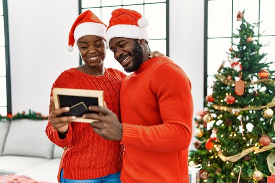 Young african american couple smiling happy and looking photo standing by christmas tree at home.
