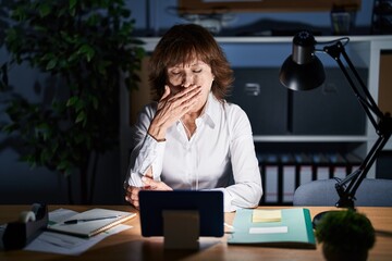 Obraz premium Middle age woman working at the office at night bored yawning tired covering mouth with hand. restless and sleepiness.