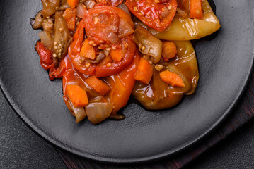 Baked vegetables, eggplant, peppers and carrots on a black plate on concrete background