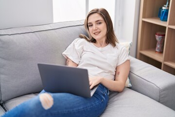Young woman using laptop lying on sofa at home
