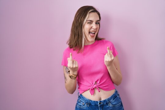 Blonde caucasian woman standing over pink background showing middle finger doing fuck you bad expression, provocation and rude attitude. screaming excited