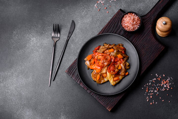 Baked vegetables, eggplant, peppers and carrots on a black plate on concrete background