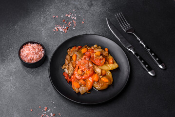 Baked vegetables, eggplant, peppers and carrots on a black plate on concrete background