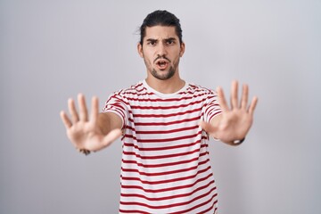 Naklejka premium Hispanic man with long hair standing over isolated background doing stop gesture with hands palms, angry and frustration expression