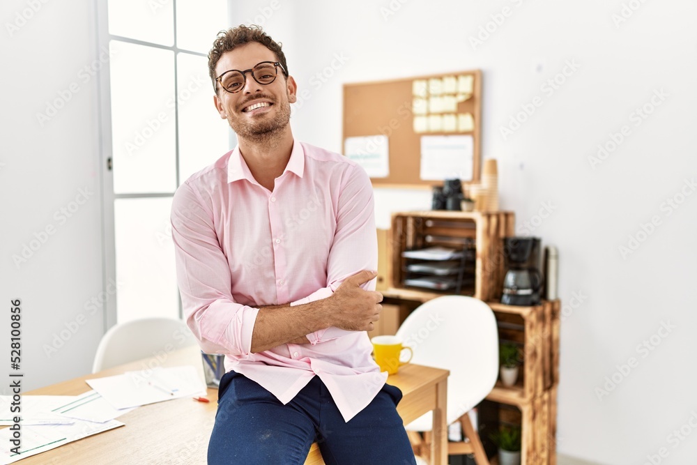 Wall mural Young hispanic man smiling confident with arms crossed gesture at office