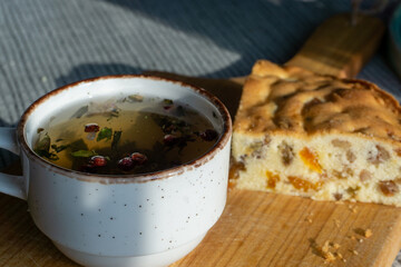 sweet cake with raisins and dried apricots, mug with herbal tea on a wooden board, natural light from the window. Horizontal photo