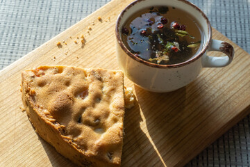 sweet cake with raisins and dried apricots, mug with herbal tea on a wooden board, natural light...