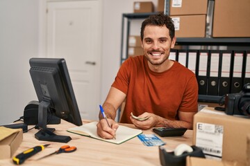 Young hispanic man ecommerce business worker writing on notebook holding chile pesos banknotes at...