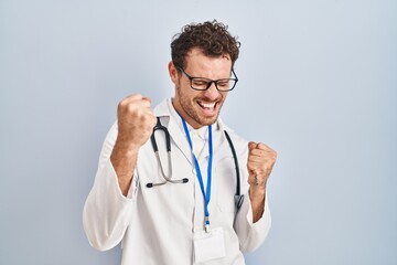 Young hispanic man wearing doctor uniform and stethoscope very happy and excited doing winner gesture with arms raised, smiling and screaming for success. celebration concept.