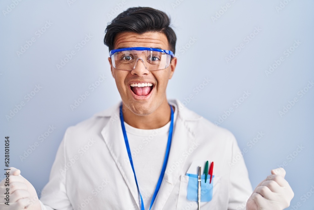 Poster Hispanic man working as scientist celebrating surprised and amazed for success with arms raised and open eyes. winner concept.