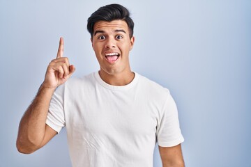Fototapeta premium Hispanic man standing over blue background pointing finger up with successful idea. exited and happy. number one.