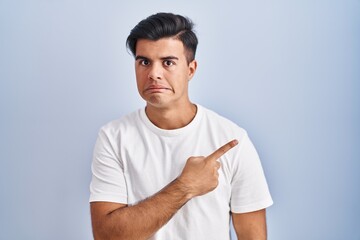 Hispanic man standing over blue background pointing aside worried and nervous with forefinger,...