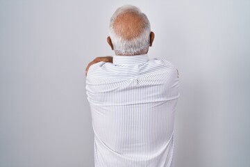 Senior man with grey hair standing over isolated background hugging oneself happy and positive from...