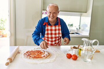 Senior man smiling confident cooking pizza at kitchen