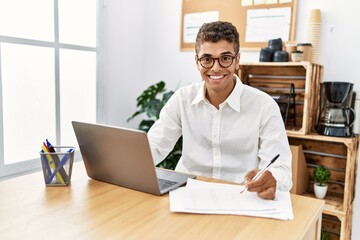 Young hispanic man working with laptop at business office