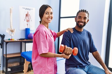 Man and woman wearing physiotherapist uniform having rehab session using dumbbell at physiotherpy...