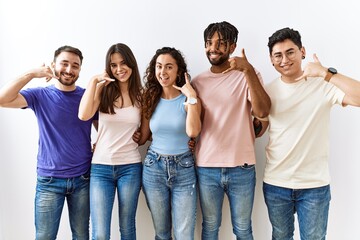 Obraz premium Group of young people standing together over isolated background smiling doing phone gesture with hand and fingers like talking on the telephone. communicating concepts.