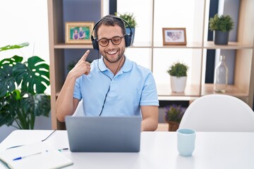 Hispanic man working using computer laptop wearing headphones smiling happy pointing with hand and finger