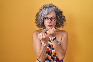 Middle age woman with grey hair standing over yellow background ready to fight with fist defense...