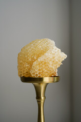 Close-up of light transparent honeycombs on a golden stand on a grey background. Natural honey and wax