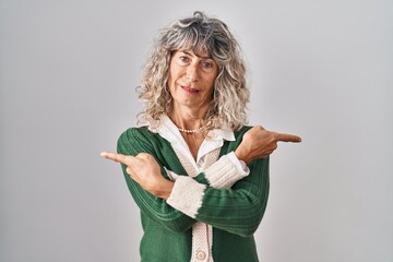 Middle age woman standing over white background pointing to both sides with fingers, different...