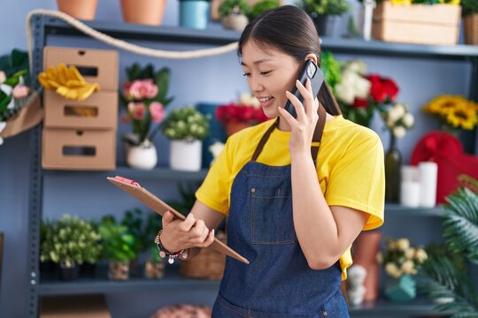 Chinese woman florist talking on smartphone reading clipboard at florist shop