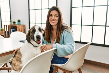 Young woman smiling confident sitting on table with dog at home