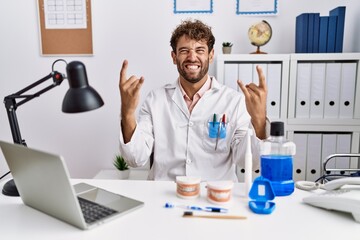 Young hispanic dentist man working at medical clinic shouting with crazy expression doing rock...