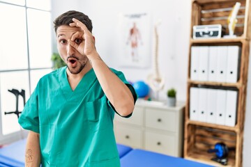 Young physiotherapist man working at pain recovery clinic doing ok gesture shocked with surprised...