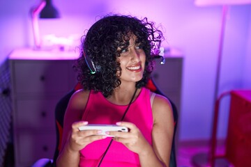 Young middle eastern woman streamer playing video game using smartphone at gaming room