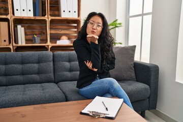 Young asian woman at consultation office looking at the camera blowing a kiss with hand on air being lovely and sexy. love expression.
