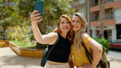 Two women hugging each other making selfie by smartphone at park