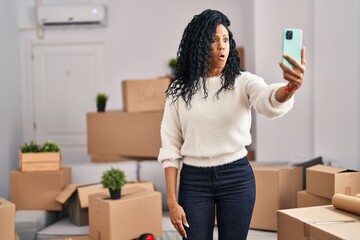 Middle age hispanic woman moving to a new home taking selfie picture scared and amazed with open...