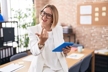 Young caucasian woman working at the office wearing glasses beckoning come here gesture with hand inviting welcoming happy and smiling - obrazy, fototapety, plakaty