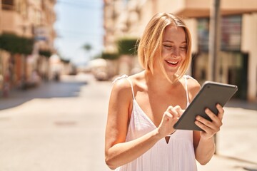 Young blonde woman smiling confident using touchpad at street