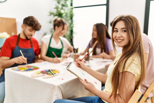 Group of people drawing sitting on the table. Young woman smiling happy looking to the camera at art studio.