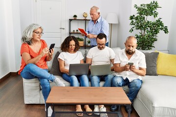 Group of middle age friends using laptop and smartphone sitting on the sofa at home.