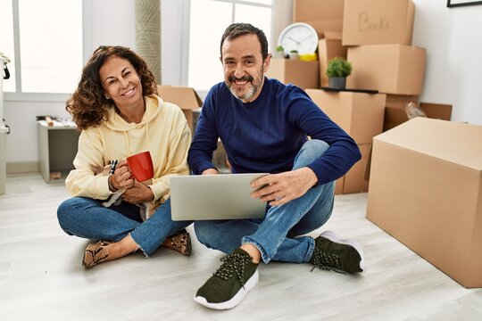 Middle age hispanic couple using laptop and drinking coffee. Sitting on the floor with dog at new home.