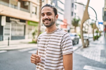 Young hispanic man smiling confident smoking cigarette at street