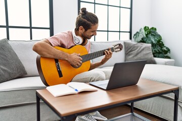 Handsome hispanic man practicing guitar with video tutorial at the living room at home