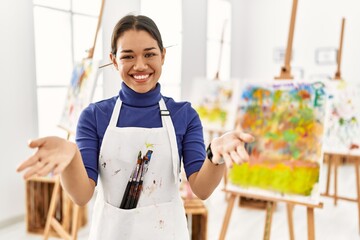 Young brunette woman at art studio smiling cheerful offering hands giving assistance and acceptance.