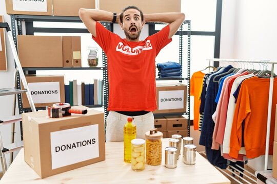 Young hispanic man wearing volunteer t shirt at donations stand crazy and scared with hands on head, afraid and surprised of shock with open mouth
