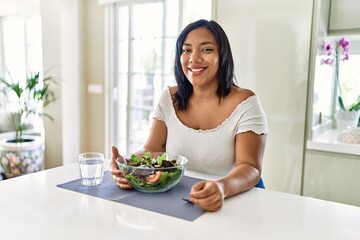 Obraz na płótnie Canvas Hispanic brunette woman eating green salad at the kitchen