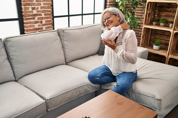 Fototapeta premium Middle age woman sitting on sofa suffering for neck pain at home
