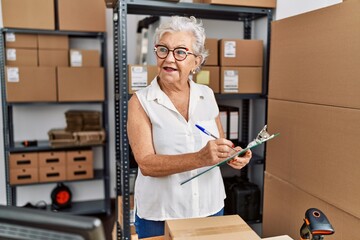 Senior grey-haired woman business worker writing on clipboard at office