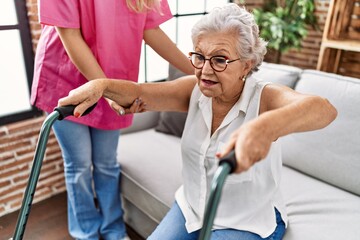 Senior grey-haired woman patient supported for nurse and walker at geriatric
