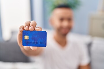 African american man holding credit card sitting on sofa at home