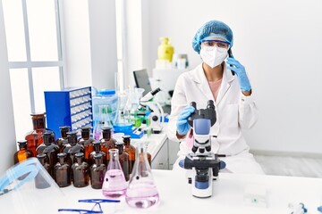 Fototapeta premium Young latin woman wearing scientist uniform talking on the smartphone at laboratory