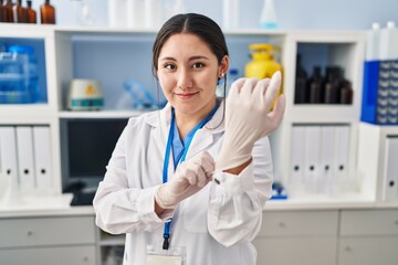 Young hispanic woman wearing scientist uniform and gloves at laboratory